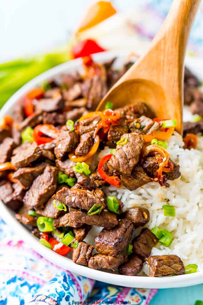 White bowl full of pepper steak with rice and a wooden spoon