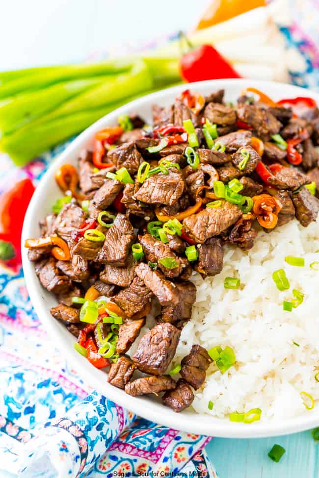 Pepper steak in a white bowl with rice garnished with green onions and sesame seeds