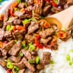 Pepper steak in a bowl with rice garnished with green onions