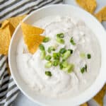 Onion dip in a white bowl topped with green onions and tortilla chips on the side