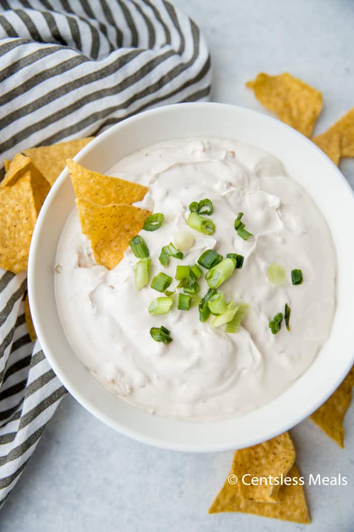 Onion dip in a white bowl topped with green onions and tortilla chips on the side