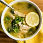 Chicken kale soup in a white bowl garnished with parsley and a lemon slice