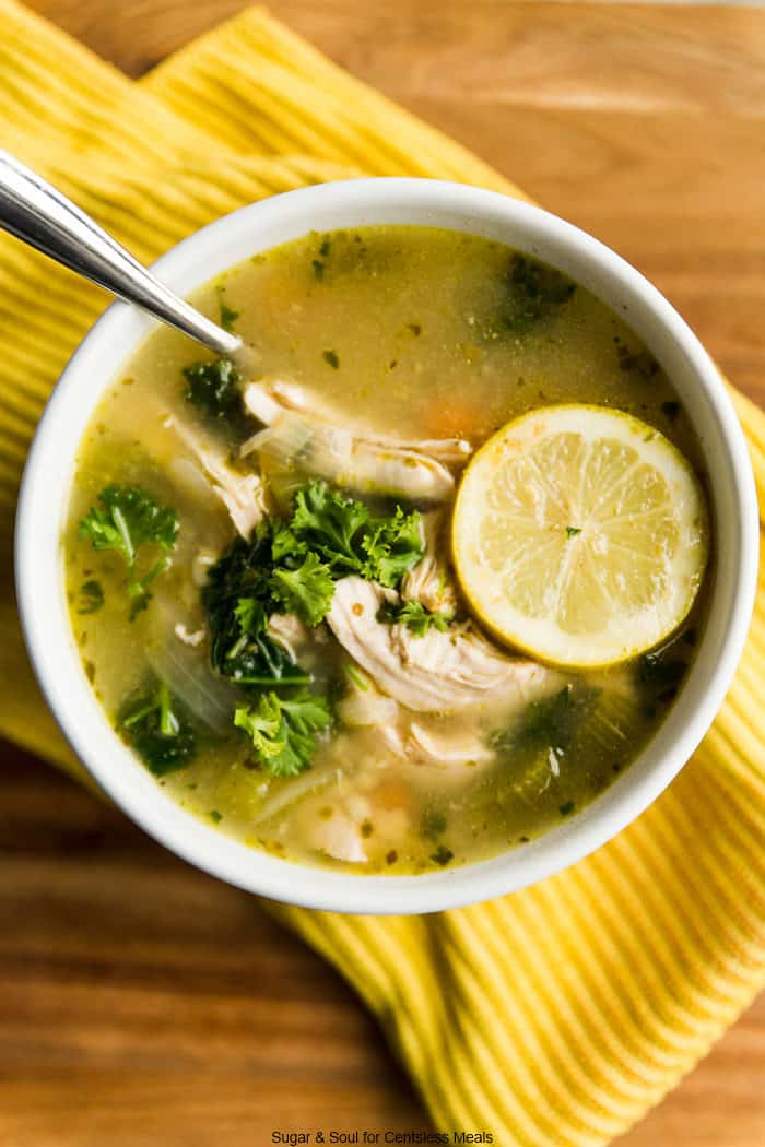Chicken kale soup in a white bowl garnished with parsley and a lemon slice