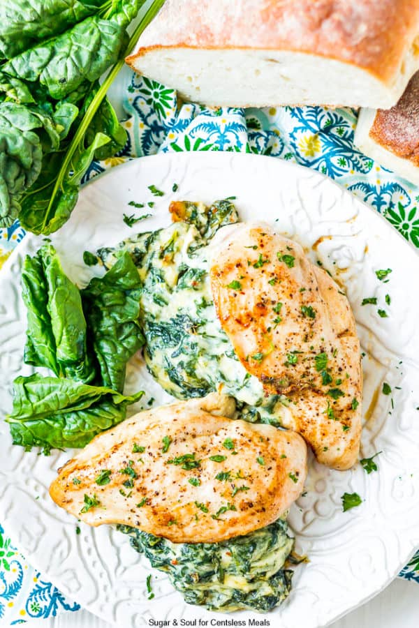 Spinach stuffed chicken on a plate with spinach and bread on the side