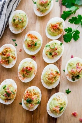 avocado deviled eggs being served on a light wood plate garnished with chopped bacon and cilantro