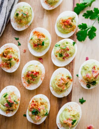 avocado deviled eggs being served on a light wood plate garnished with chopped bacon and cilantro