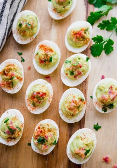 avocado deviled eggs being served on a light wood plater garnished with chopped bacon and cilantro