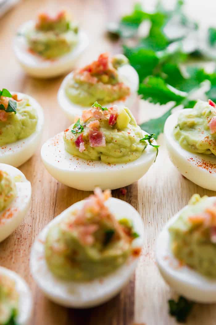 Avocado eggs on a wooden board with bacon and parsley on top