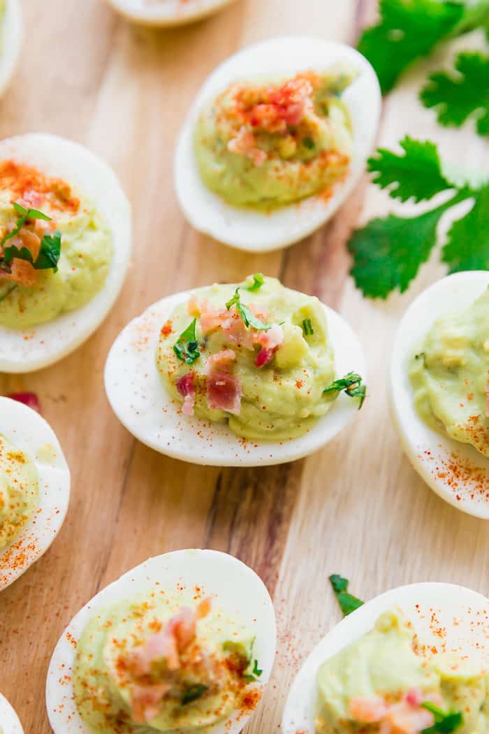 Avocado deviled eggs on a wooden board garnished with bacon and parsley