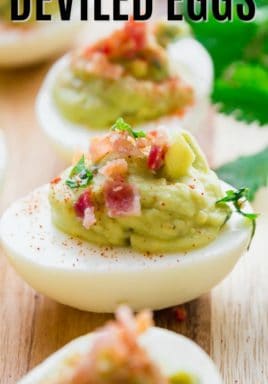 Avocado deviled eggs on a wooden board with writing