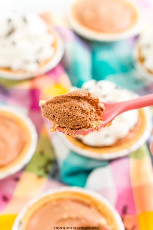 pink spoon with a bite of no bake chocolate cheesecake on it and a bunch of cheesecakes in the background.