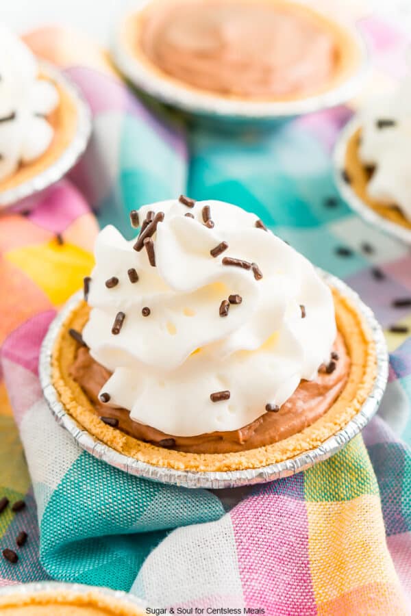 Mini No Bake Chocolate Cheesecake with whipped cream and chocolate sprinkles on a colorful checkered napkin.