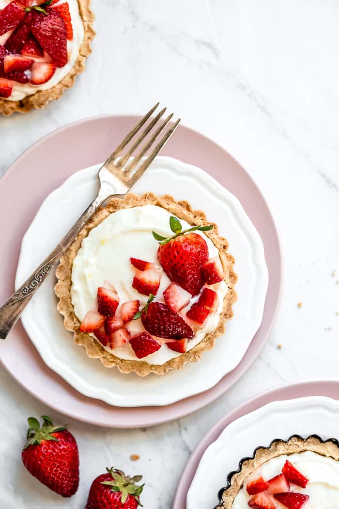 Strawberry mini tarts on plates with strawberries and a fork