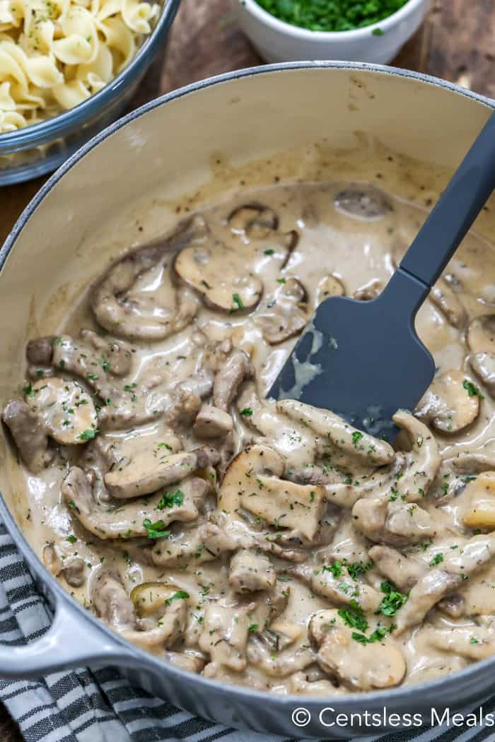 Beef stroganoff in a pot with a rubber spatula garnished with parsley