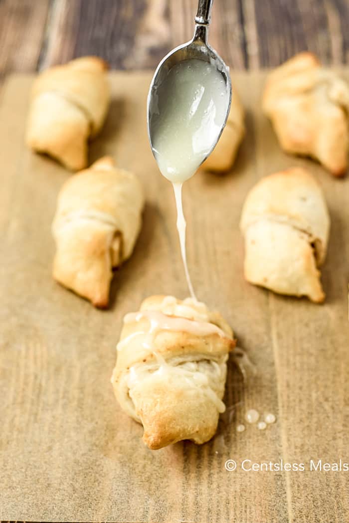 Cinnamon apple crescents on parchment with icing being drizzled on