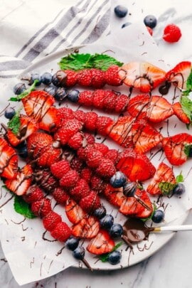 Fruit kabobs on a white plate drizzled with chocolate