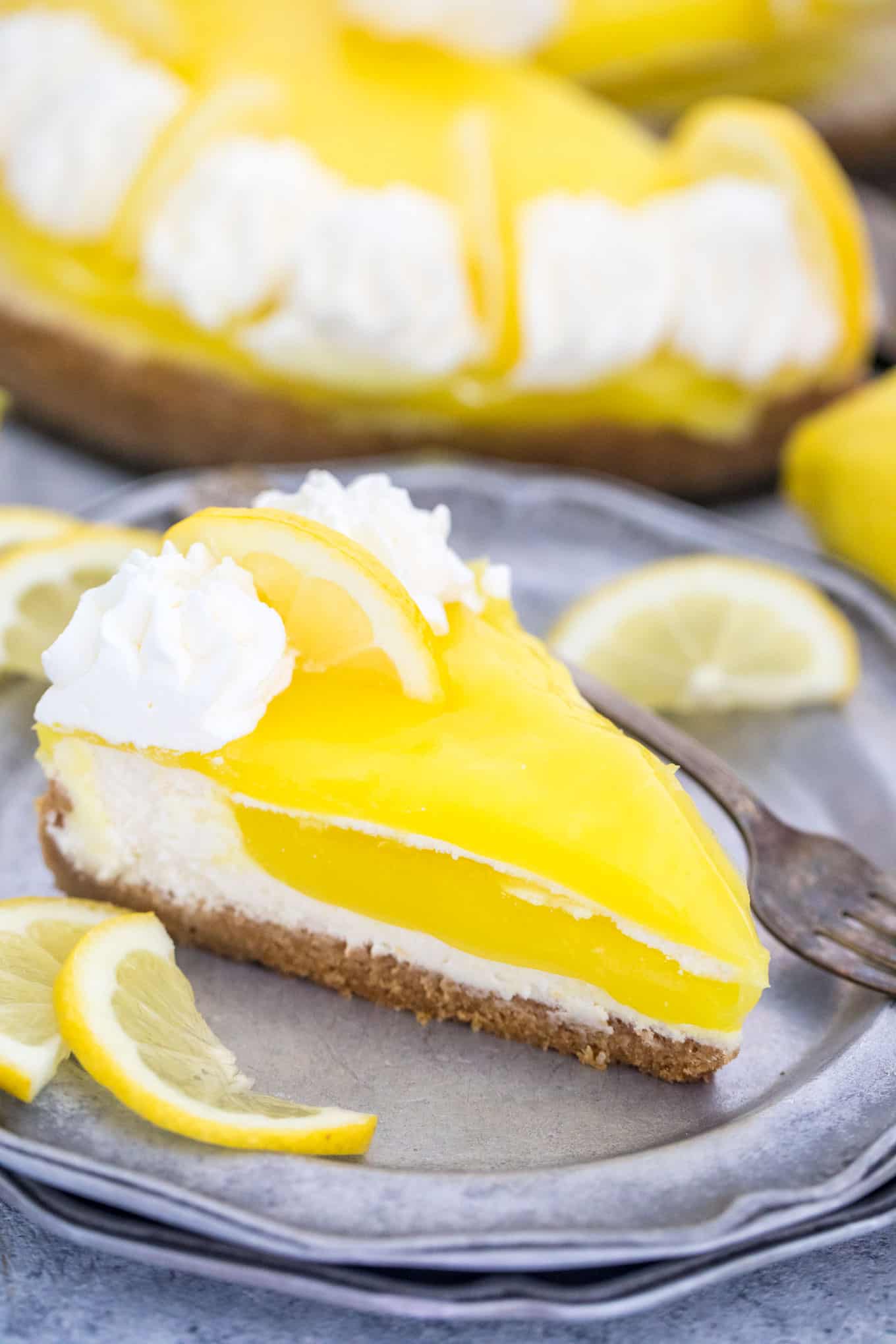 Piece of lemon cheesecake on a plate with a fork and lemon slices