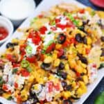 Chicken nachos on a white plate with sour cream and tomatoes on top