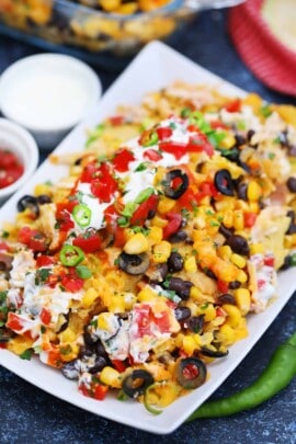 Chicken nachos on a white plate with sour cream and tomatoes on top