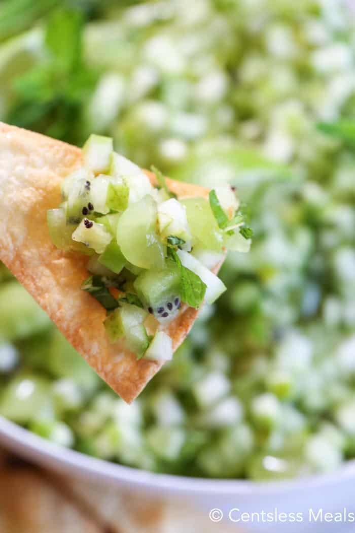 Mojito fruit salsa on a chip with a bowl of mojito fruit salsa in the background