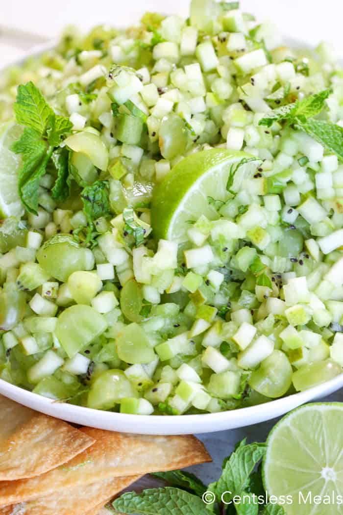 Mojito fruit salsa in a white bowl garnished with mint leaves and lime wedges