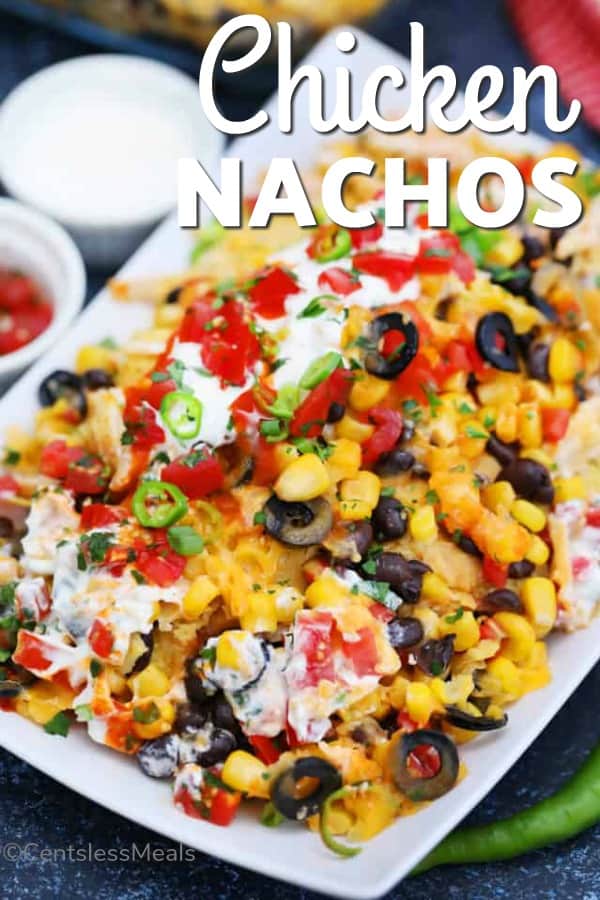 Chicken nachos on a white plate with sour cream and tomatoes and writing