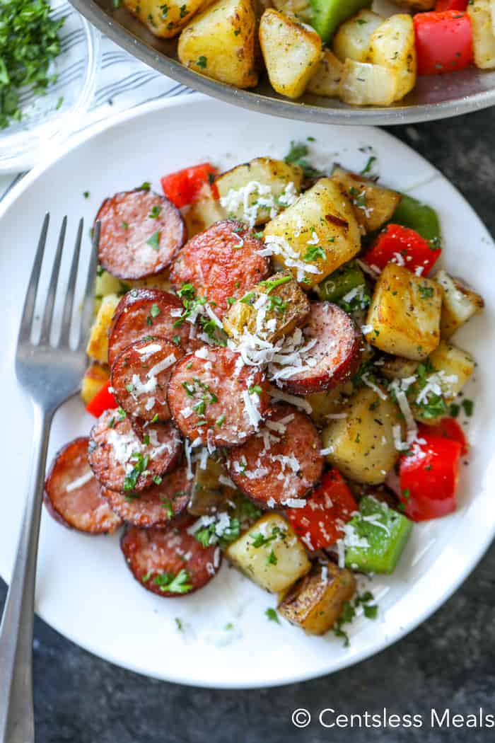 Sausage and potato Skillet on a white plate with a fork garnished with parsley and cheese