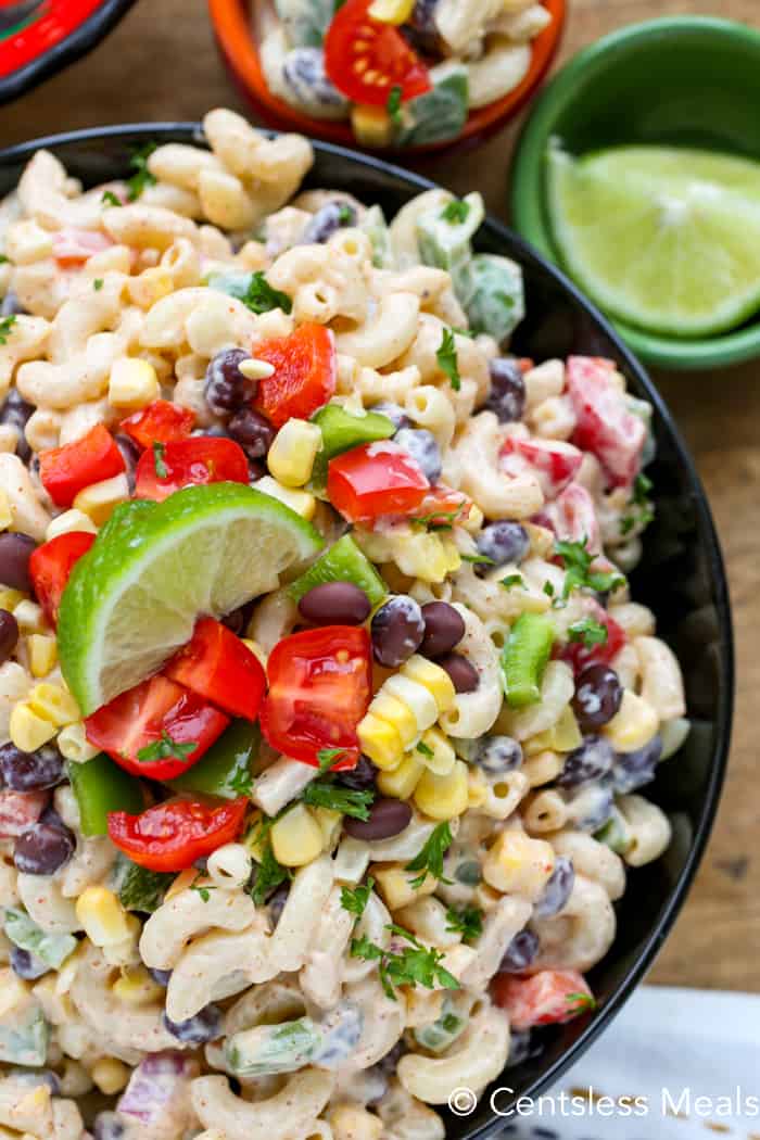 Southwestern macaroni salad in a black bowl with tomato and lime as garnish