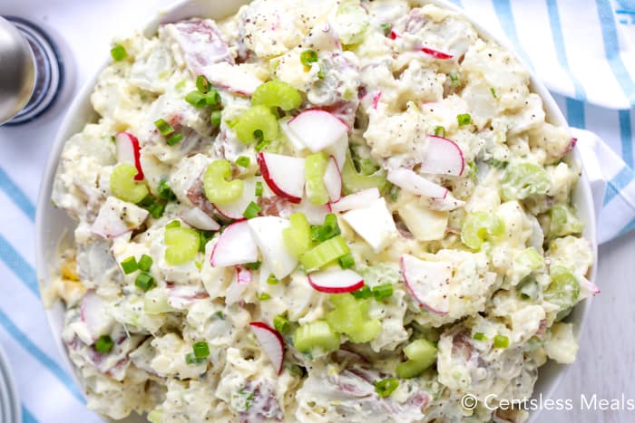 Creamy potato salad in a bowl garnished with green onions celery and radishes