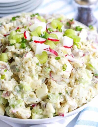 Creamy potato salad in a white bowl garnished with radishes and celery