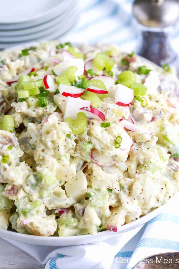 Creamy potato salad in a white bowl garnished with radishes and celery