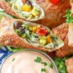 Avocado egg rolls on a plate with dip in a glass bowl