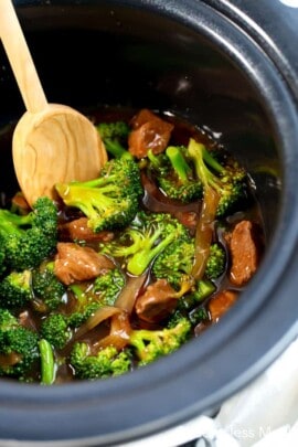 Crockpot beef and broccoli in a crock pot with a wooden spoon