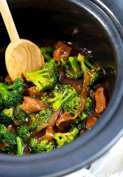 Crockpot beef and broccoli in a crock pot with a wooden spoon