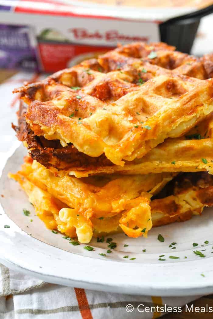 Mac and cheese waffles piled up together on a white plate and garnished with parsley.