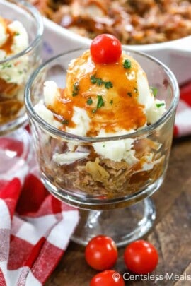 Pulled pork sundae in a glass dish garnished with parsley and a cherry tomato