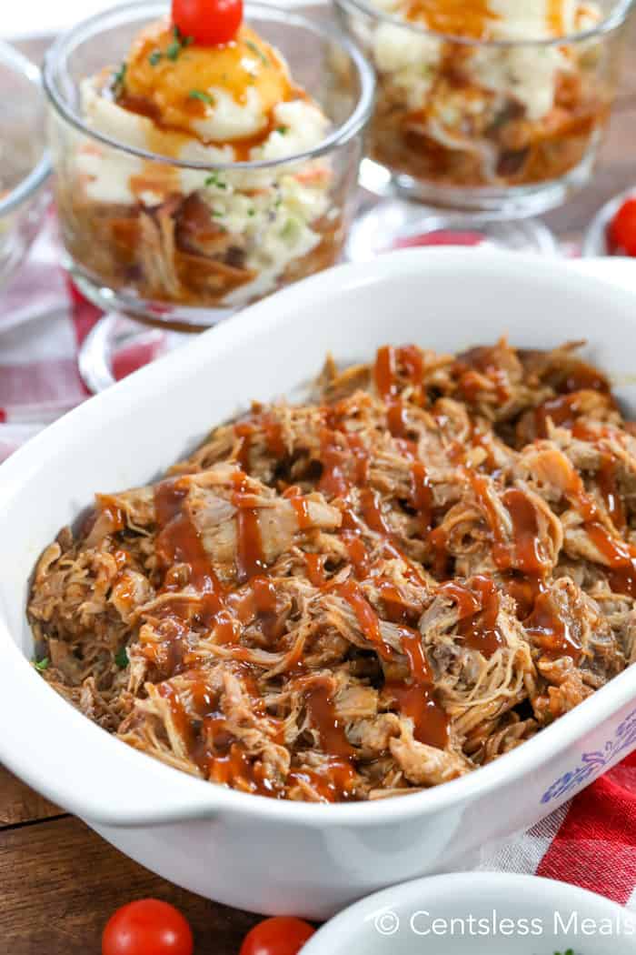 Pulled pork with sauce in a white casserole dish with pulled pork Sundaes in the background