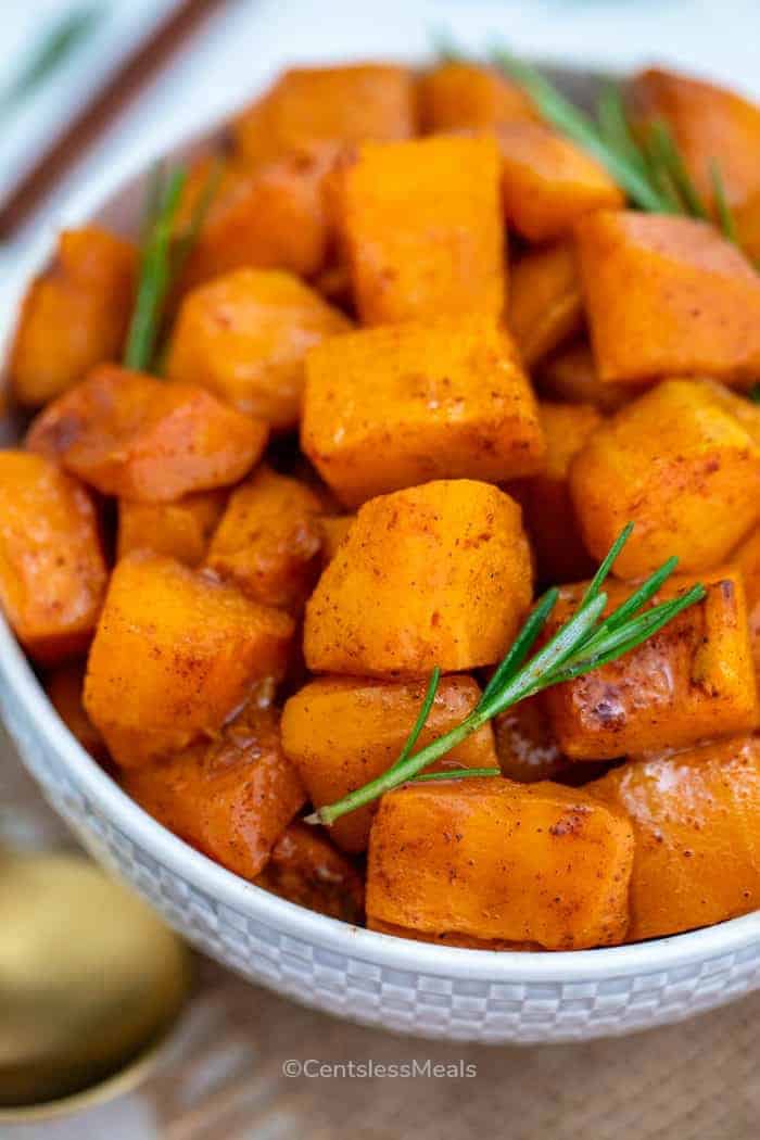 Roasted butternut squash in a white bowl garnished with rosemary