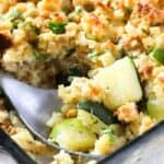 Stuffing zucchini casserole in a clear casserole dish with a spoon