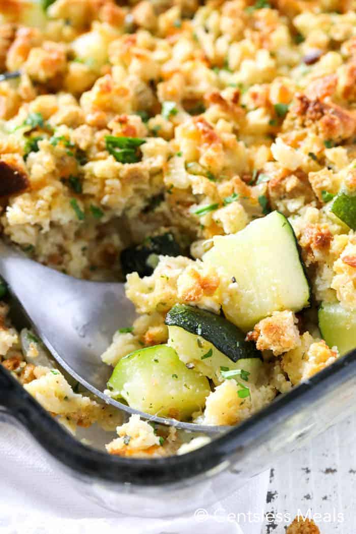 Stuffing zucchini casserole in a clear casserole dish with a spoon