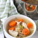 Chicken rice soup in a white bowl with a spoon and the pot of soup on the side