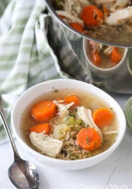 Chicken rice soup in a white bowl with a spoon and the pot of soup on the side