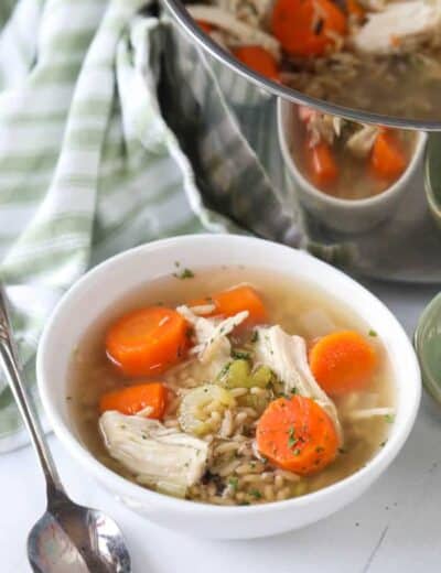 Chicken rice soup in a white bowl with a spoon and the pot of soup on the side