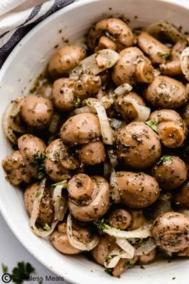 Marinated mushrooms in a bowl with onion slivers