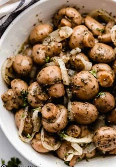 Marinated mushrooms in a bowl with onion slivers