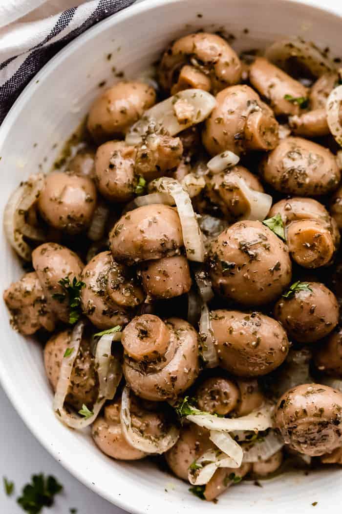 marinated mushrooms in a white bowl with onion and parsley