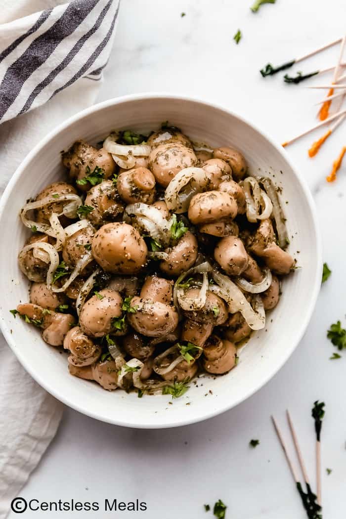 Marinated mushrooms in a white bowl on a marble board