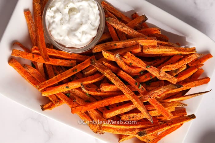 Sweet potato fries on a white plate with a bowl of aioli