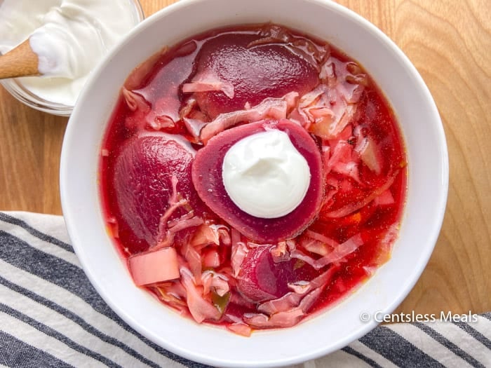 A bowl of colorful Beet Borscht with a small dish of sour cream on the side.