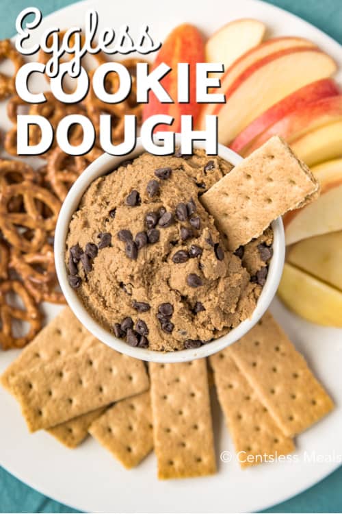 Eggless Cookie Dough in a white bowl and on a plate surrounded by fruit, crackers and pretzels, with writing